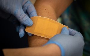  Nurse with blue gloves putting large bandaid on a student's arm
